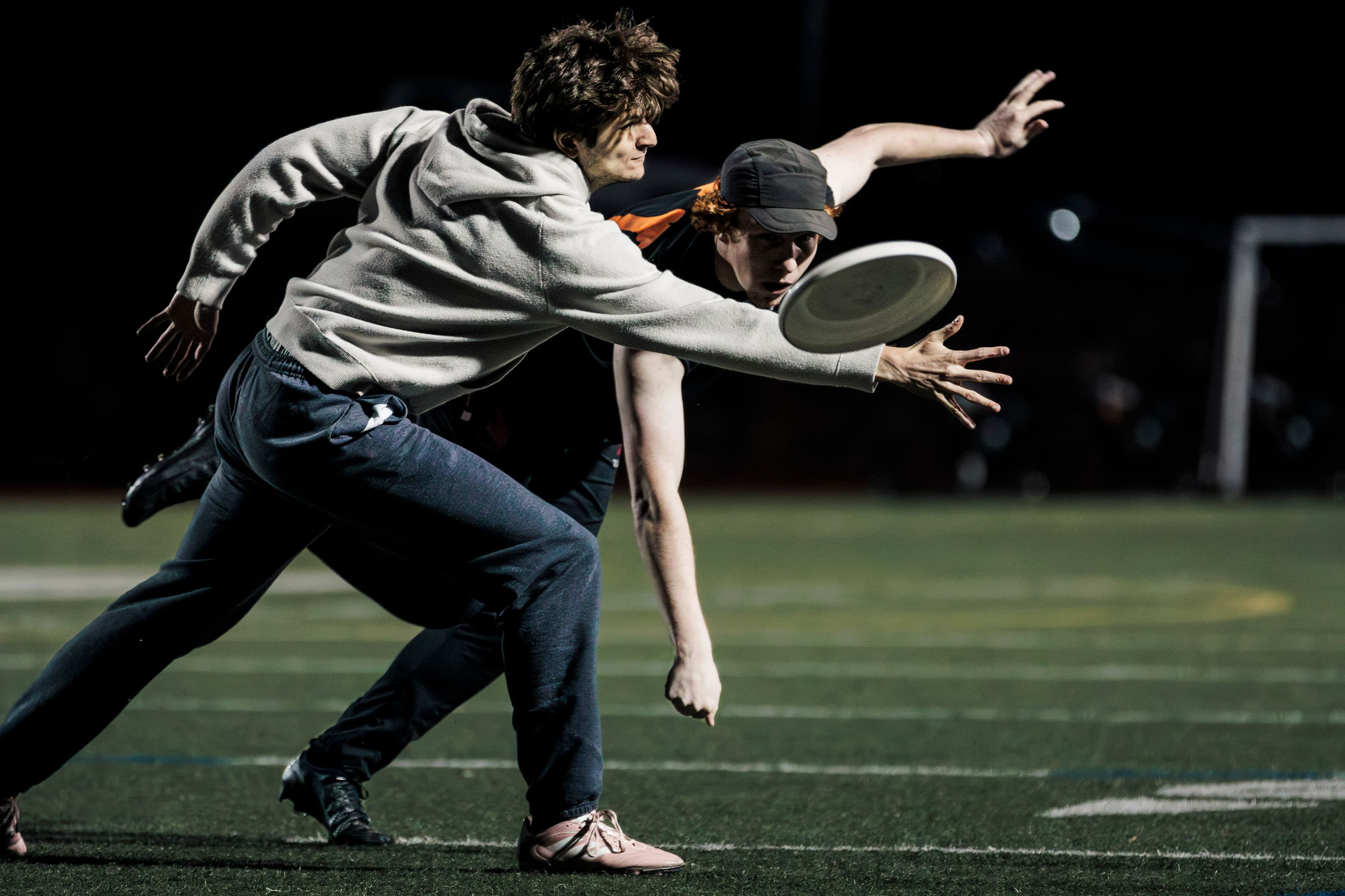 A player reaching for a flying disc under stadium lights.