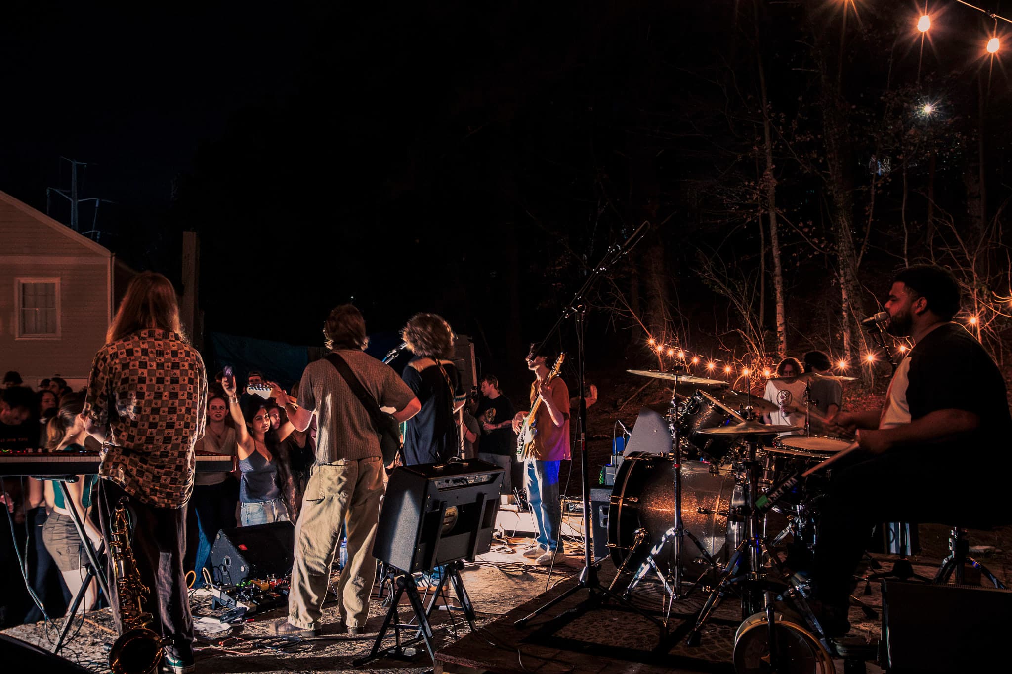 A band performs beneath string lights as the crowd gathers around the outdoor stage.