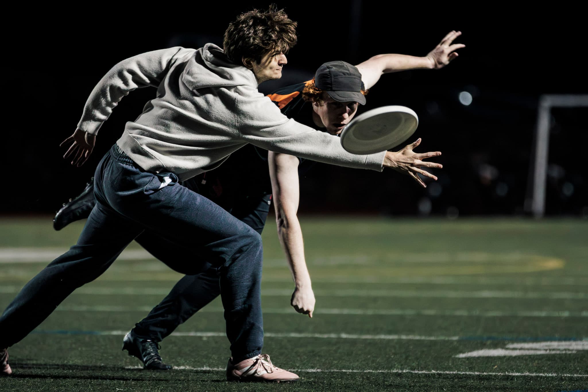 A player reaching for a flying disc under stadium lights.