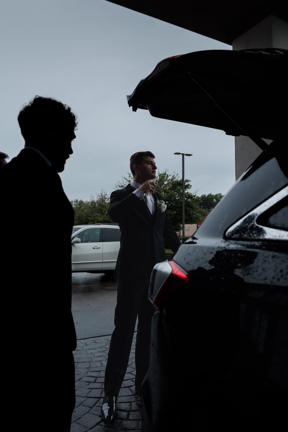 A silhouetted guest stands near a car as the wedding party prepares to leave.