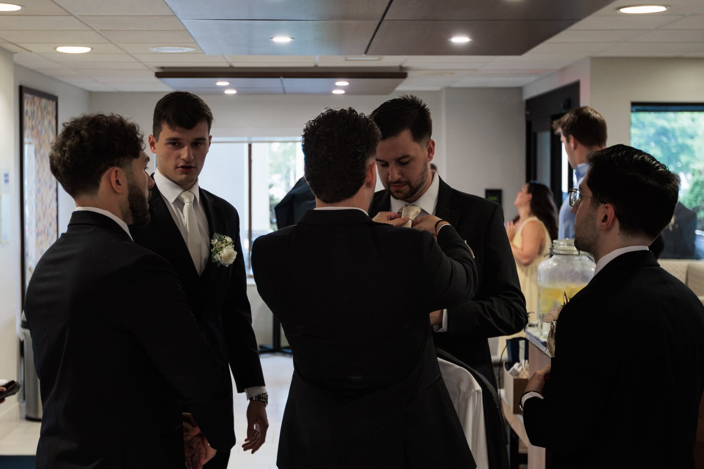 Several men gather closely as they help with final suit adjustments.