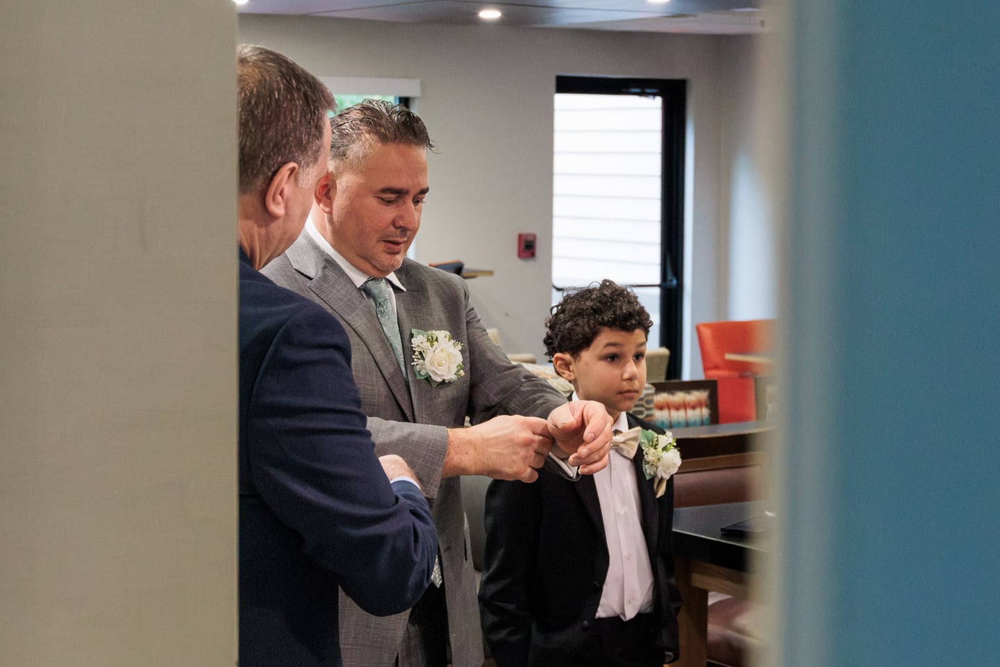A man in a gray suit helps adjust a younger guest's formalwear.
