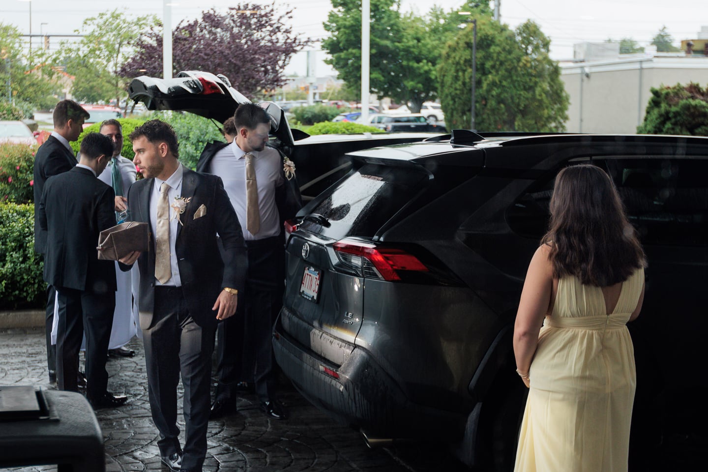 Wedding guests gather around a parked car outside the hotel.