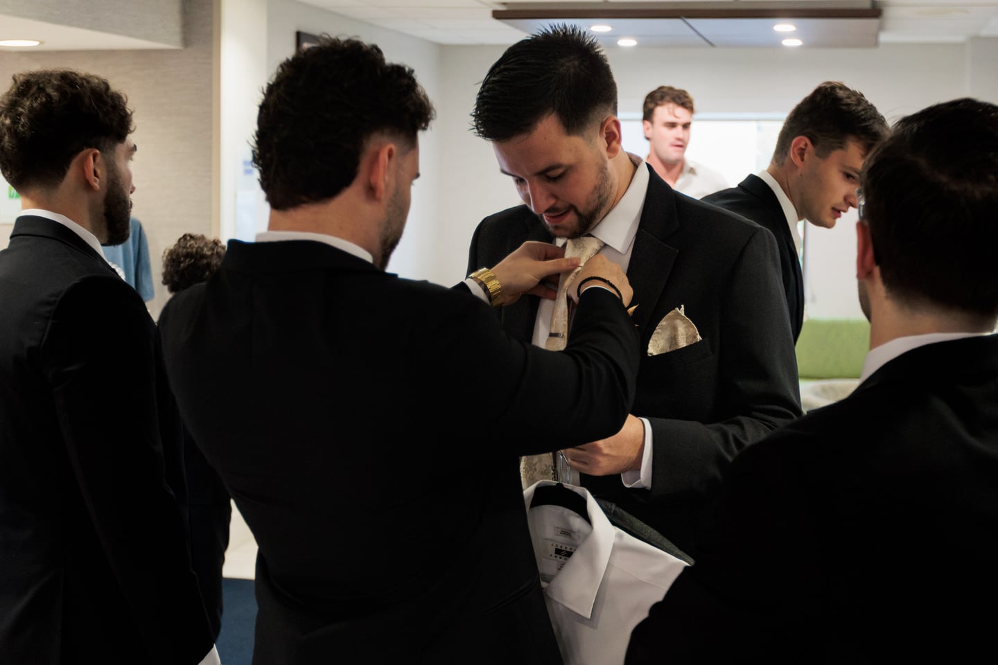 A wedding party member adjusts a boutonniere on a man's lapel.