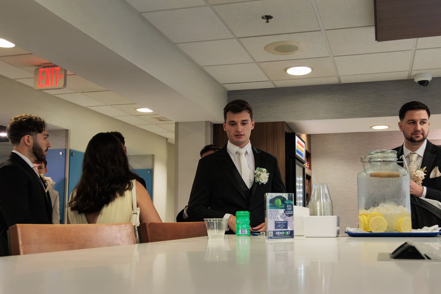A suited wedding guest stands near a table during the getting-ready gathering.
