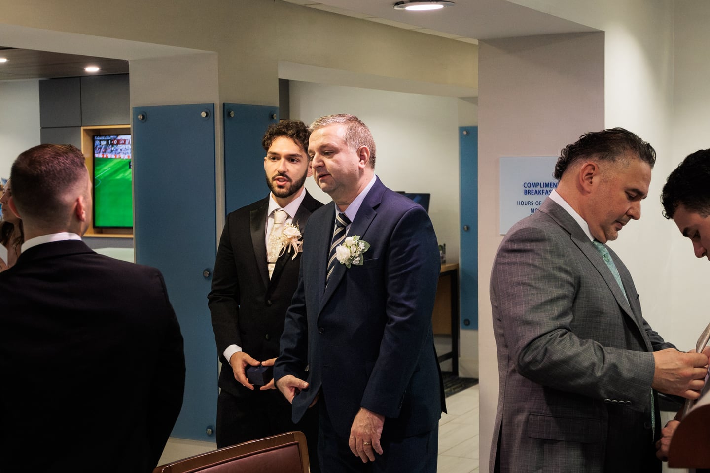 Two men in formalwear stand together while others prepare nearby.