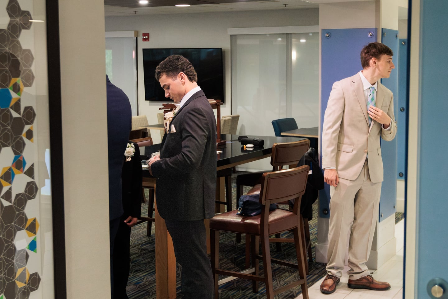 Two men in formalwear prepare near a mirror and doorway.