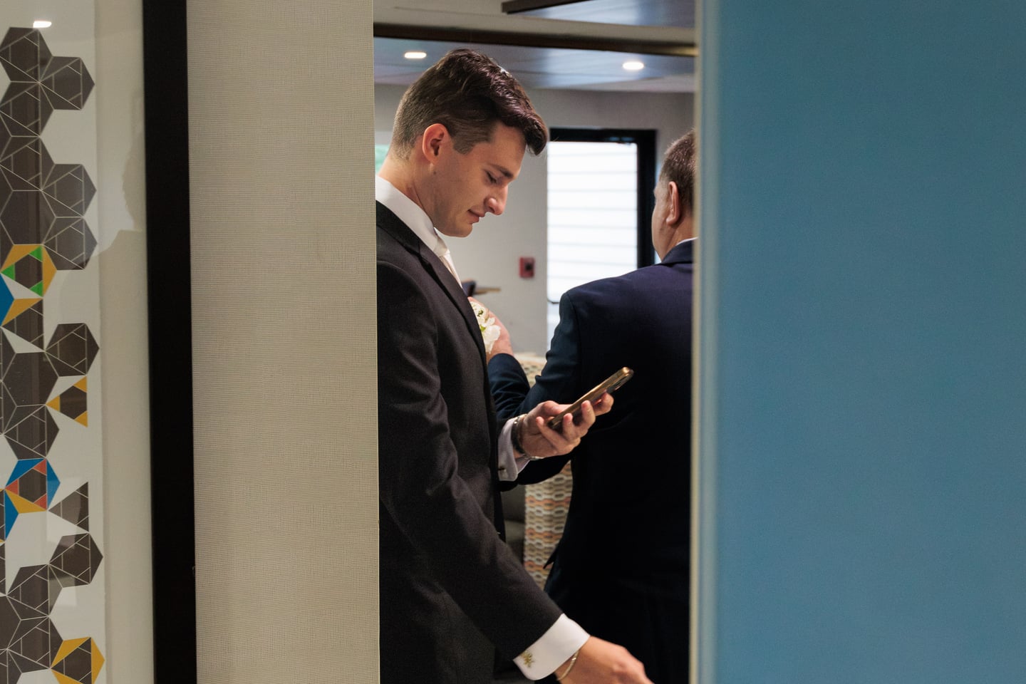 A man in a dark suit checks his phone during wedding preparations.