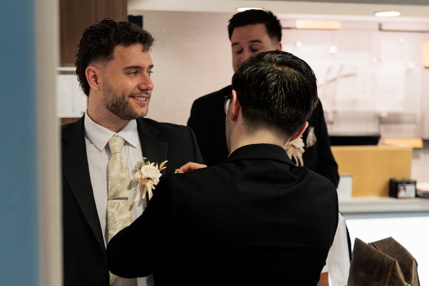 A wedding party member adjusts another man's boutonniere before the ceremony.