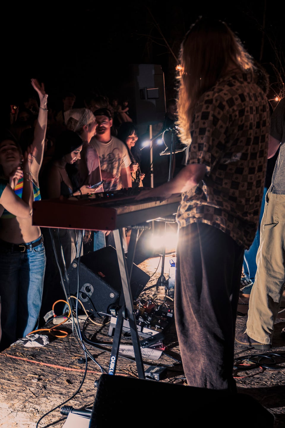 A keyboardist performs beside audience members gathered tightly around the outdoor stage.