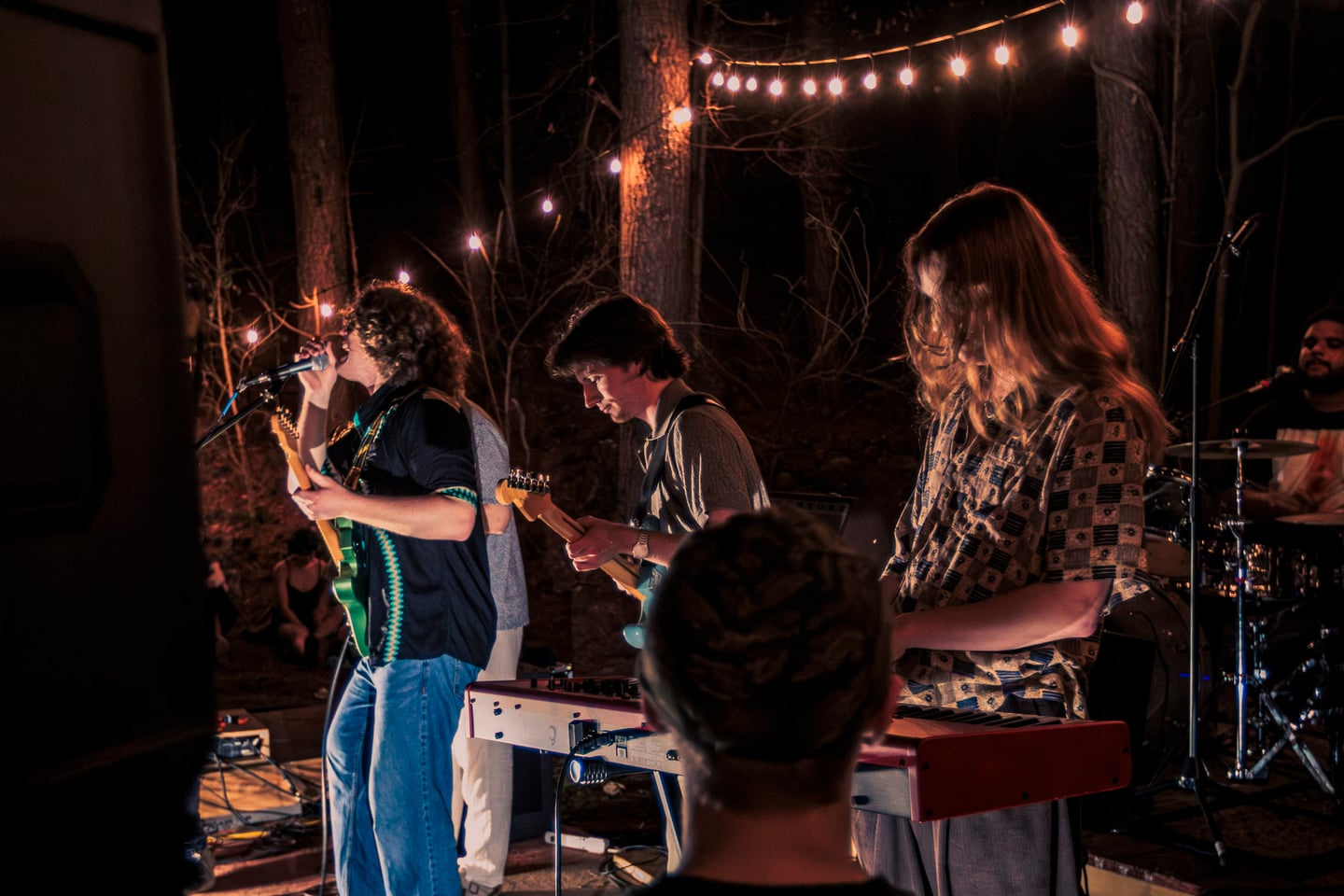 A guitarist sings while another guitarist, the keyboardist, and drummer perform beside him.