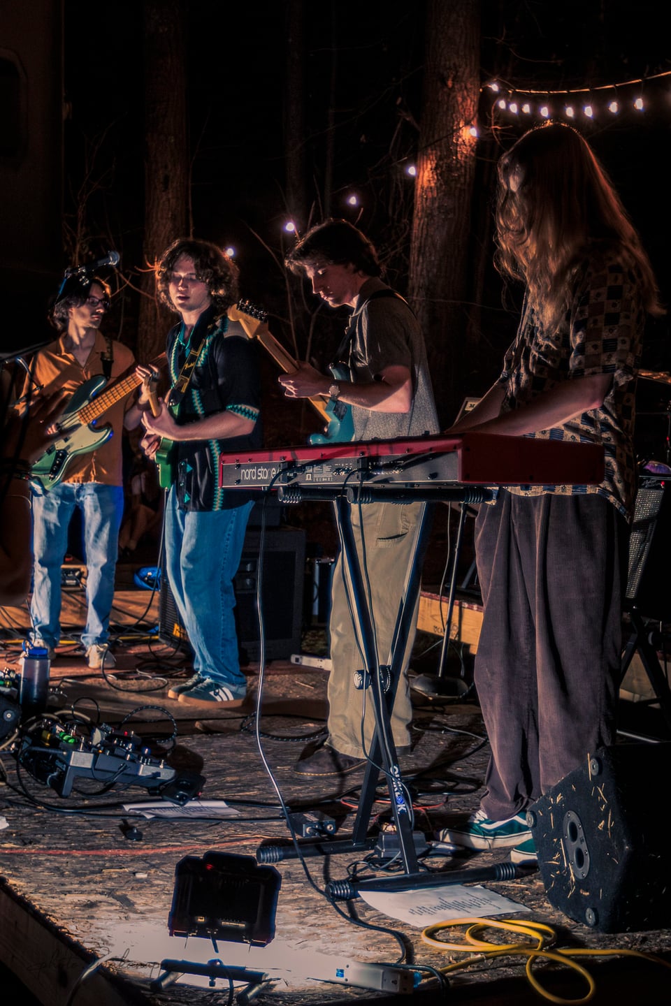 A keyboardist plays alongside a bassist and two guitarists on the outdoor stage.