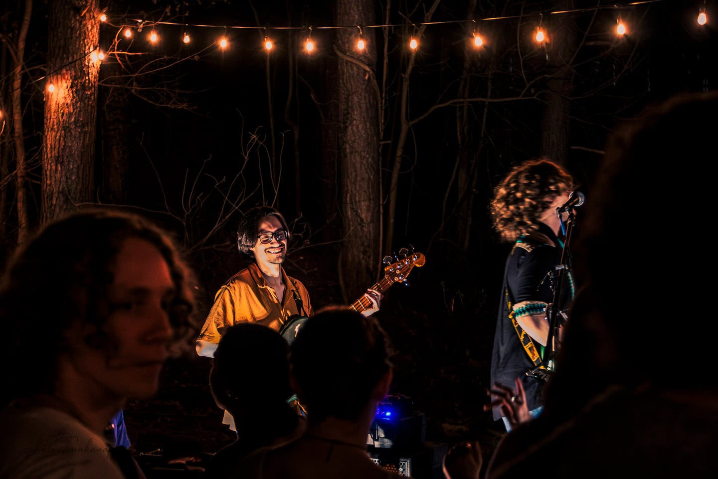 The bassist smiles toward a guitarist at the microphone as the crowd watches from close range.