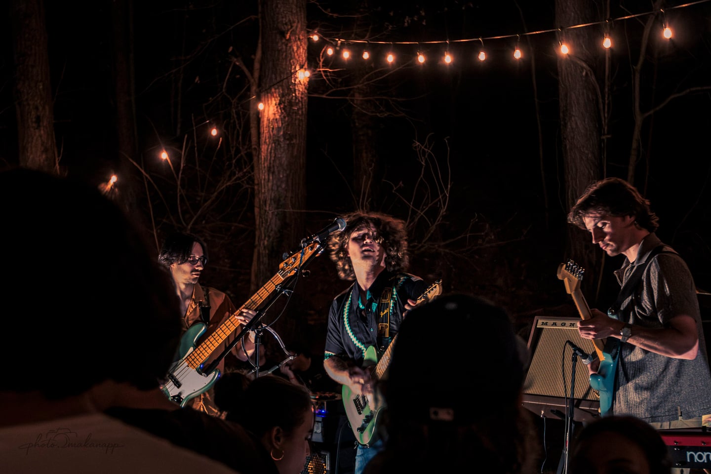 Three guitarists perform across the stage with audience silhouettes in the foreground.