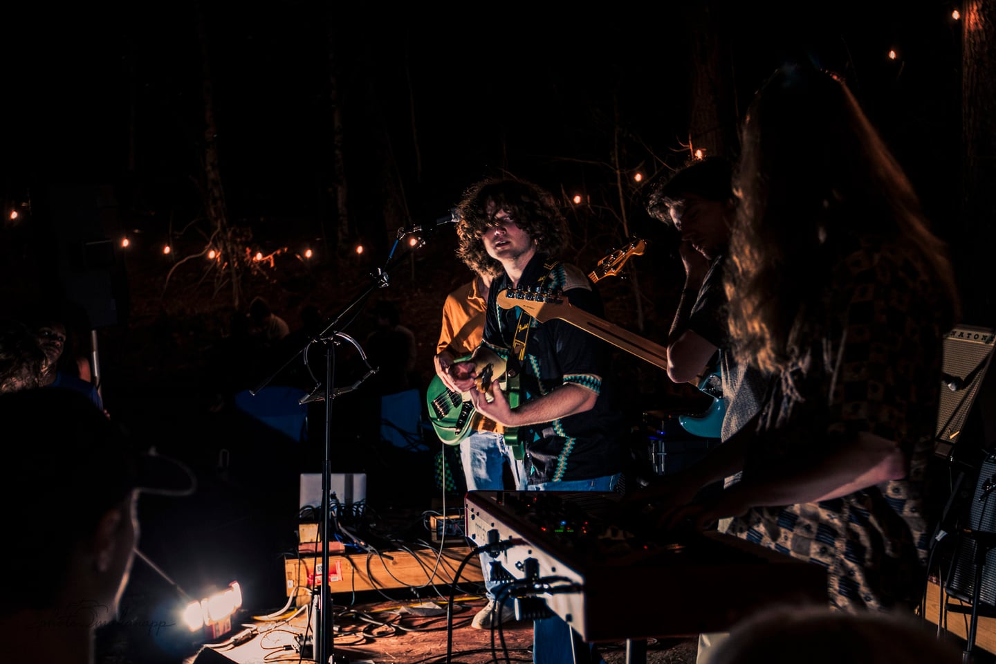 A guitarist plays at center stage between the bassist, keyboardist, and another guitarist.