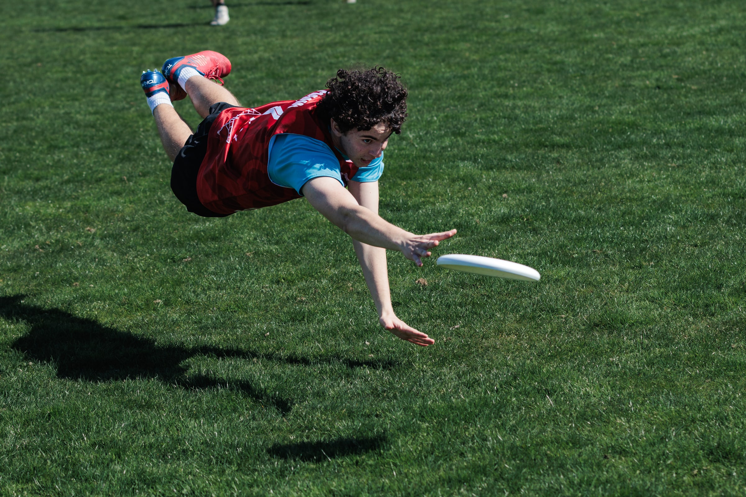 Red-clad player lays out at full extension toward a low disc.