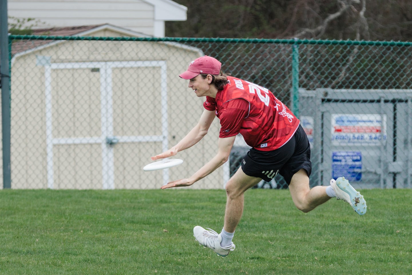 Red-clad handler releases a low forehand while running across the field.