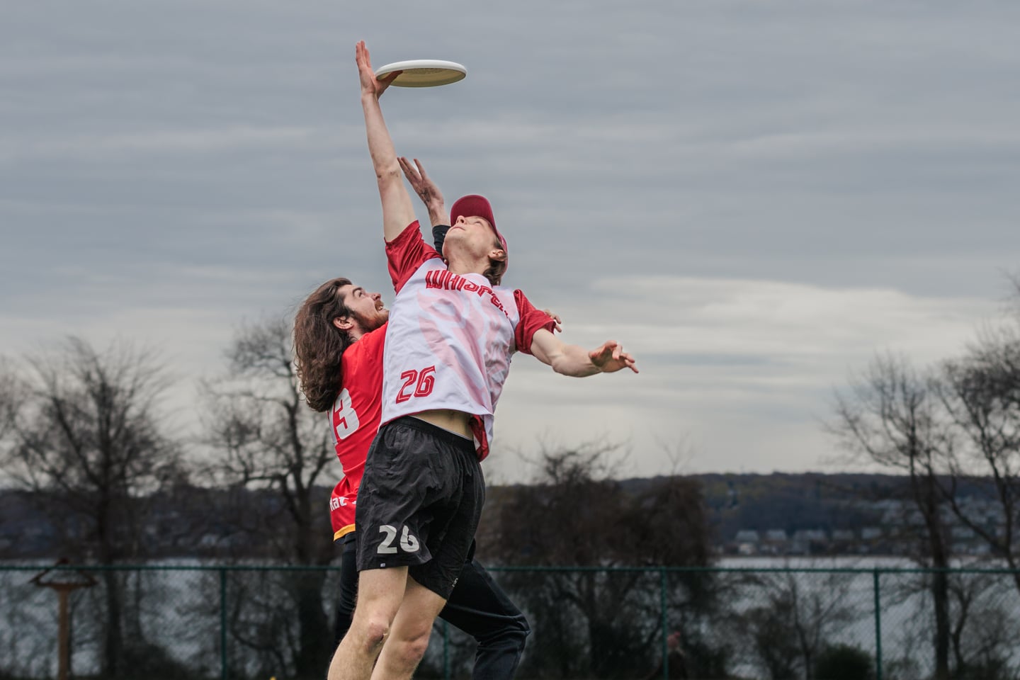 White-clad receiver reaches one-handed for a high disc over a red-clad defender.