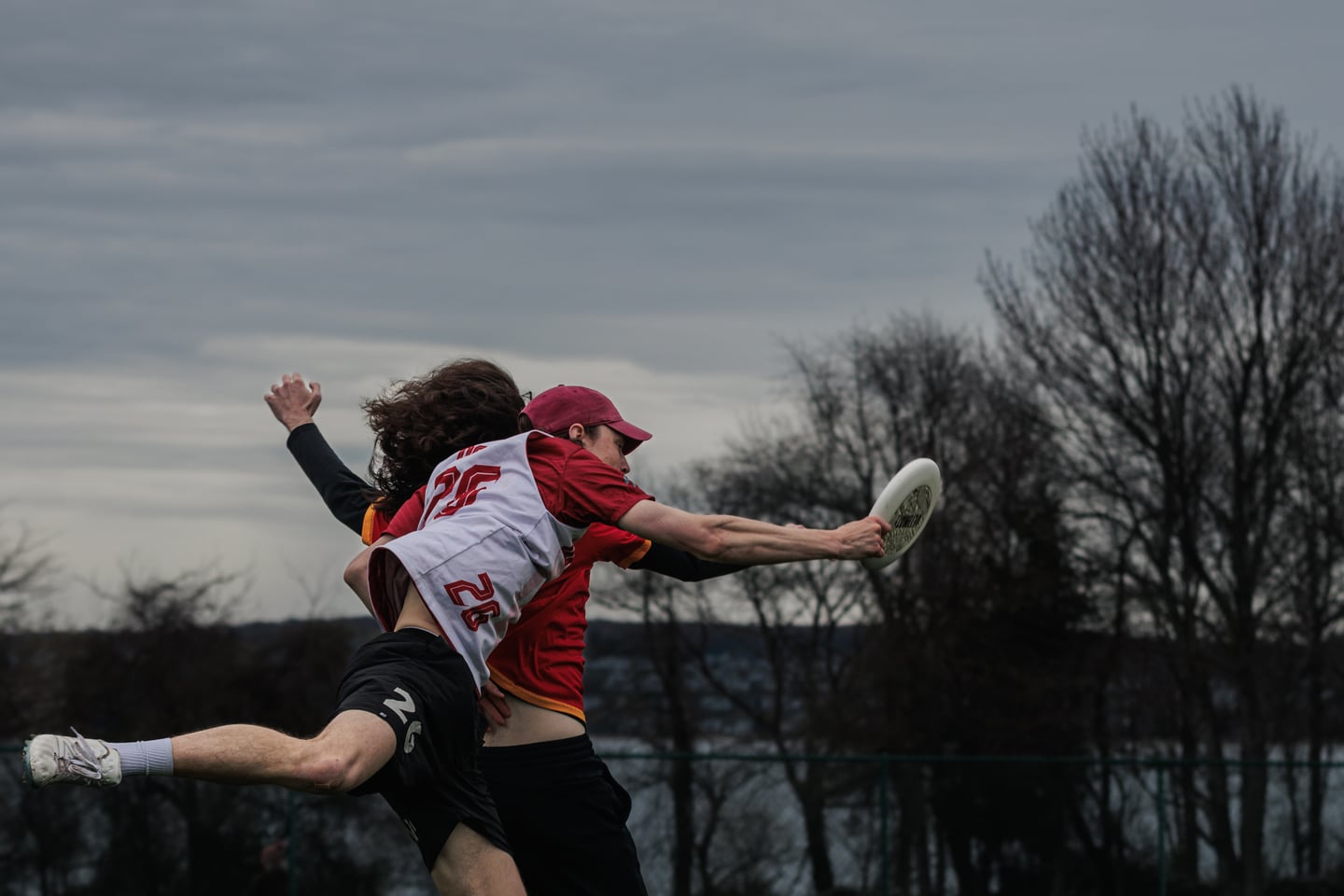 White-clad player secures the disc one-handed while colliding with a red-clad defender.