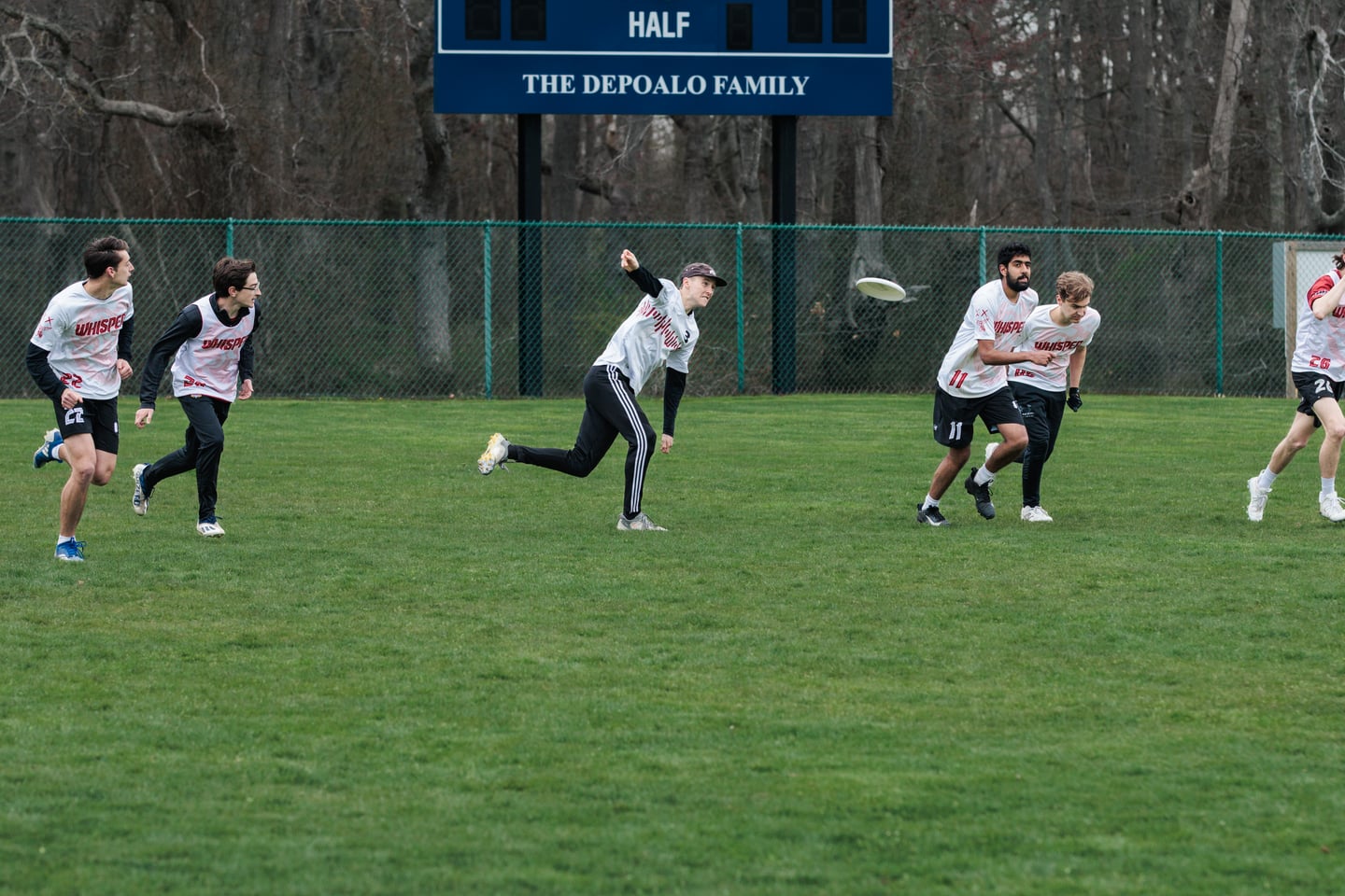 White-clad thrower sends the disc downfield as teammates begin their cuts.