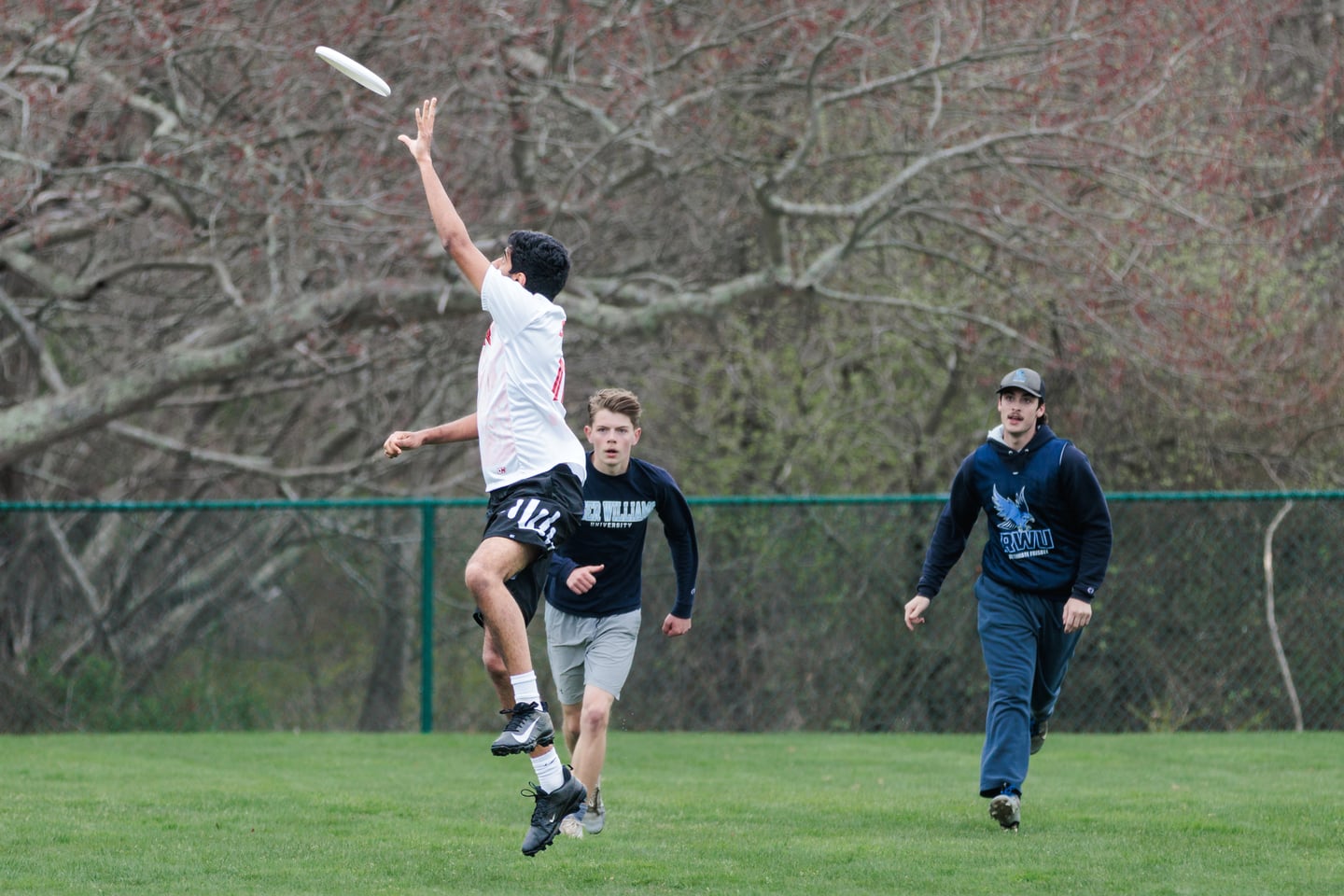 White-clad receiver leaps above a dark-clad defender for a high disc.