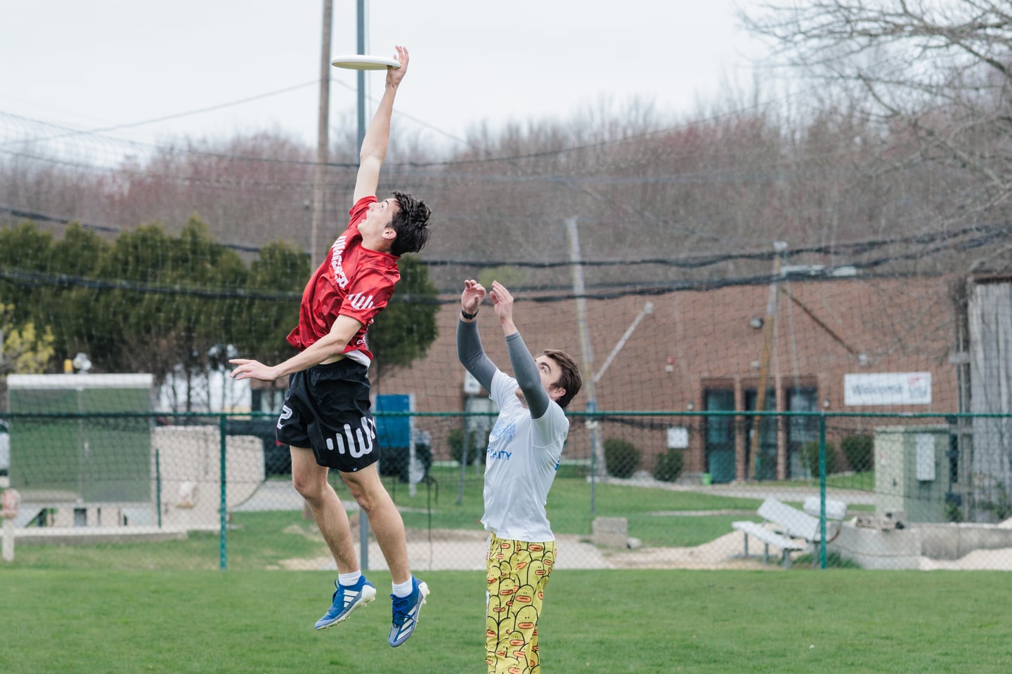 Red-clad receiver jumps above a gray-clad defender to secure the disc one-handed.