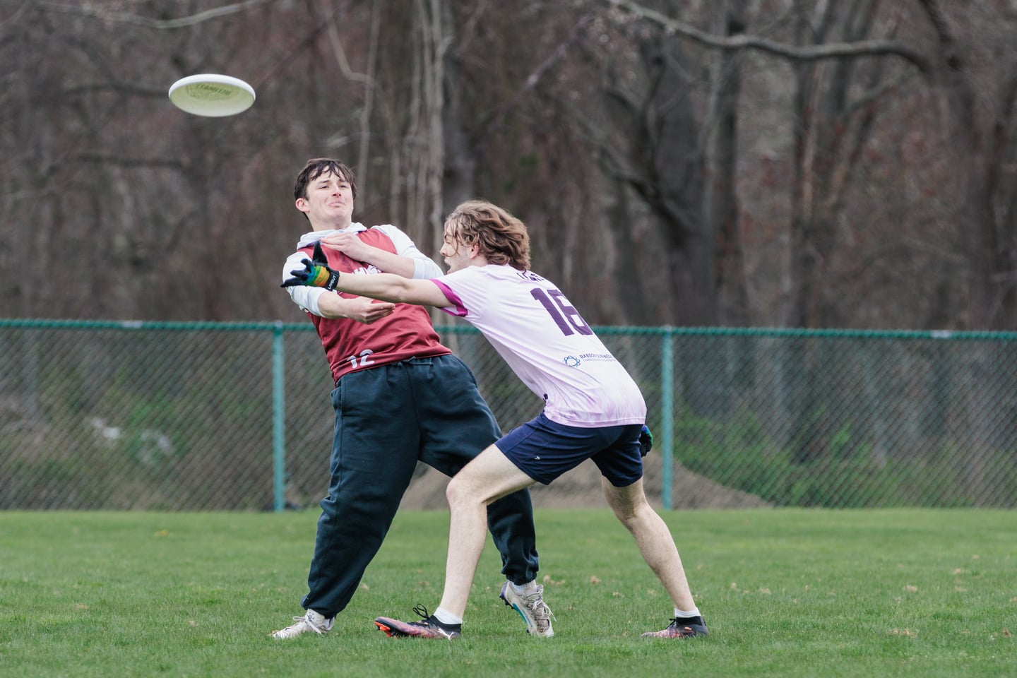 Maroon-clad receiver catches a high disc with a white-clad defender at their shoulder.