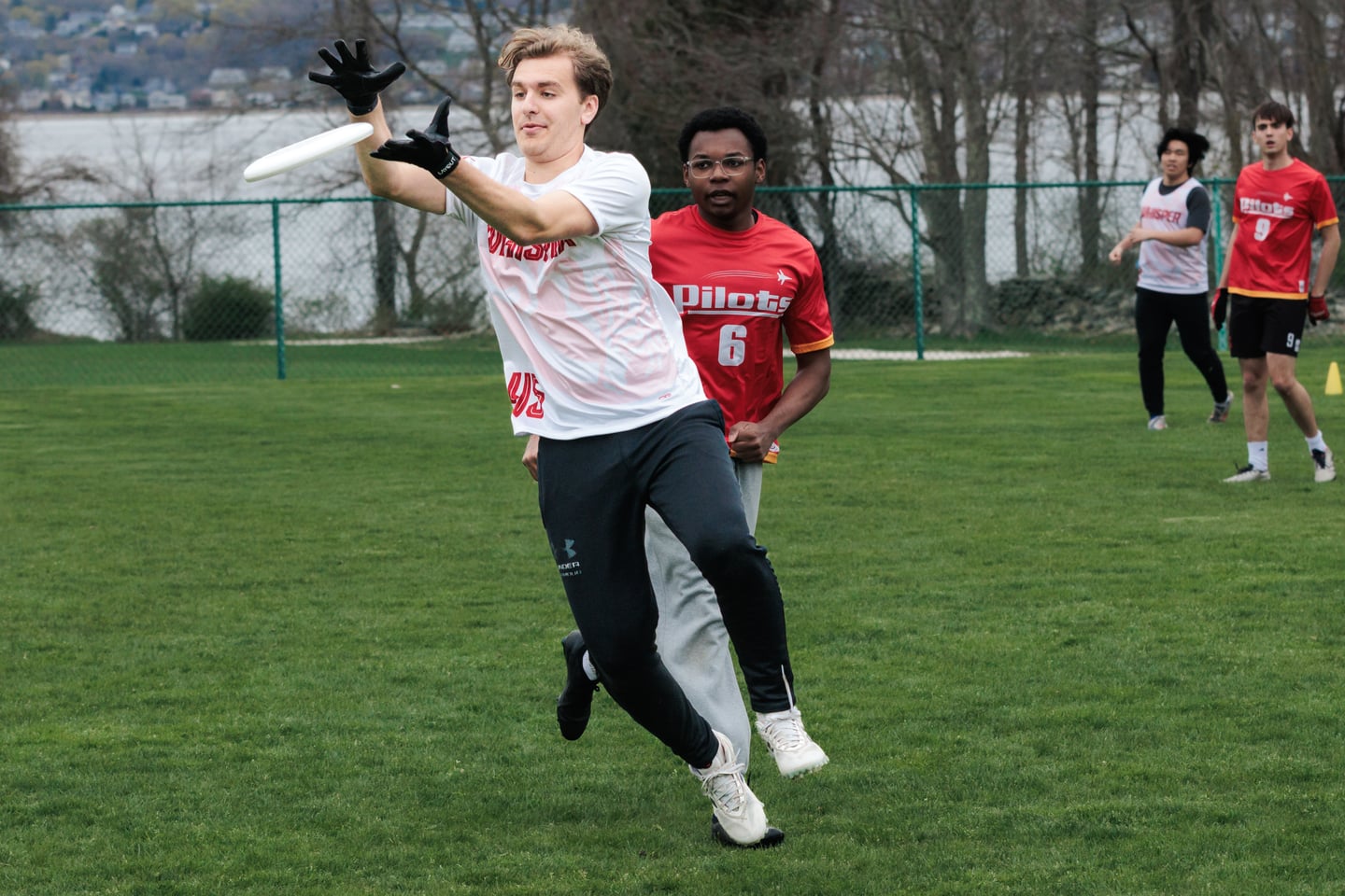 White-clad receiver reaches forward for the disc while a red-clad defender follows.