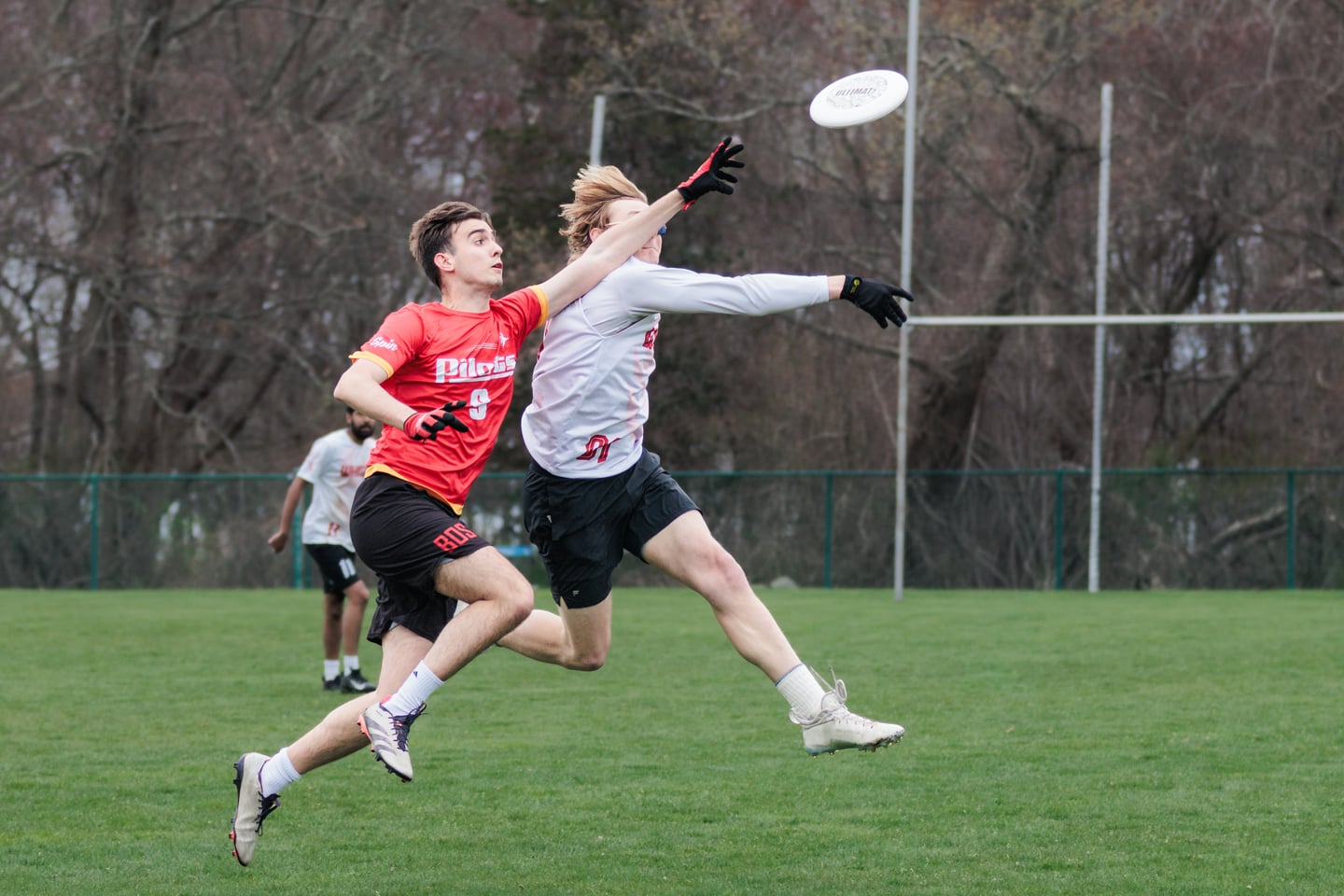 White-clad receiver races a red-clad defender toward a floating disc.