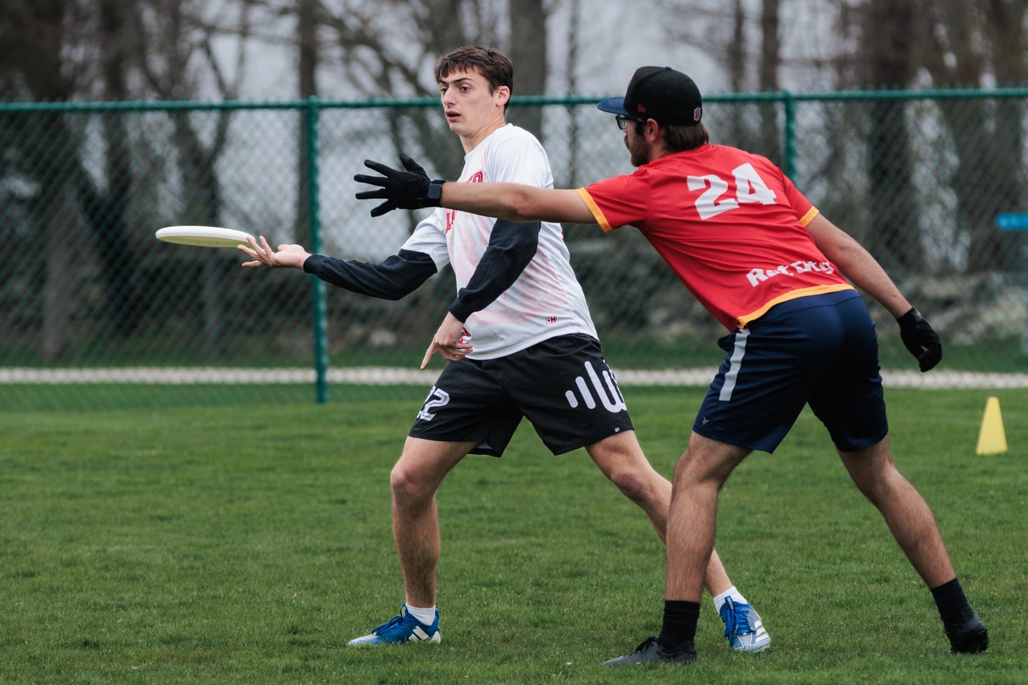 White-clad handler releases a forehand while a red-clad marker reaches across.