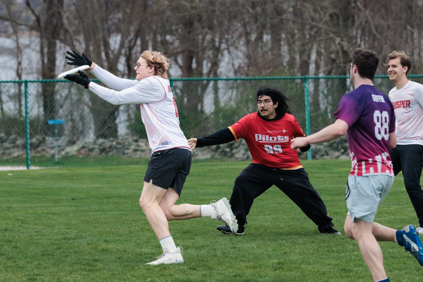 White-clad receiver catches the disc as a red-clad defender reaches from behind.