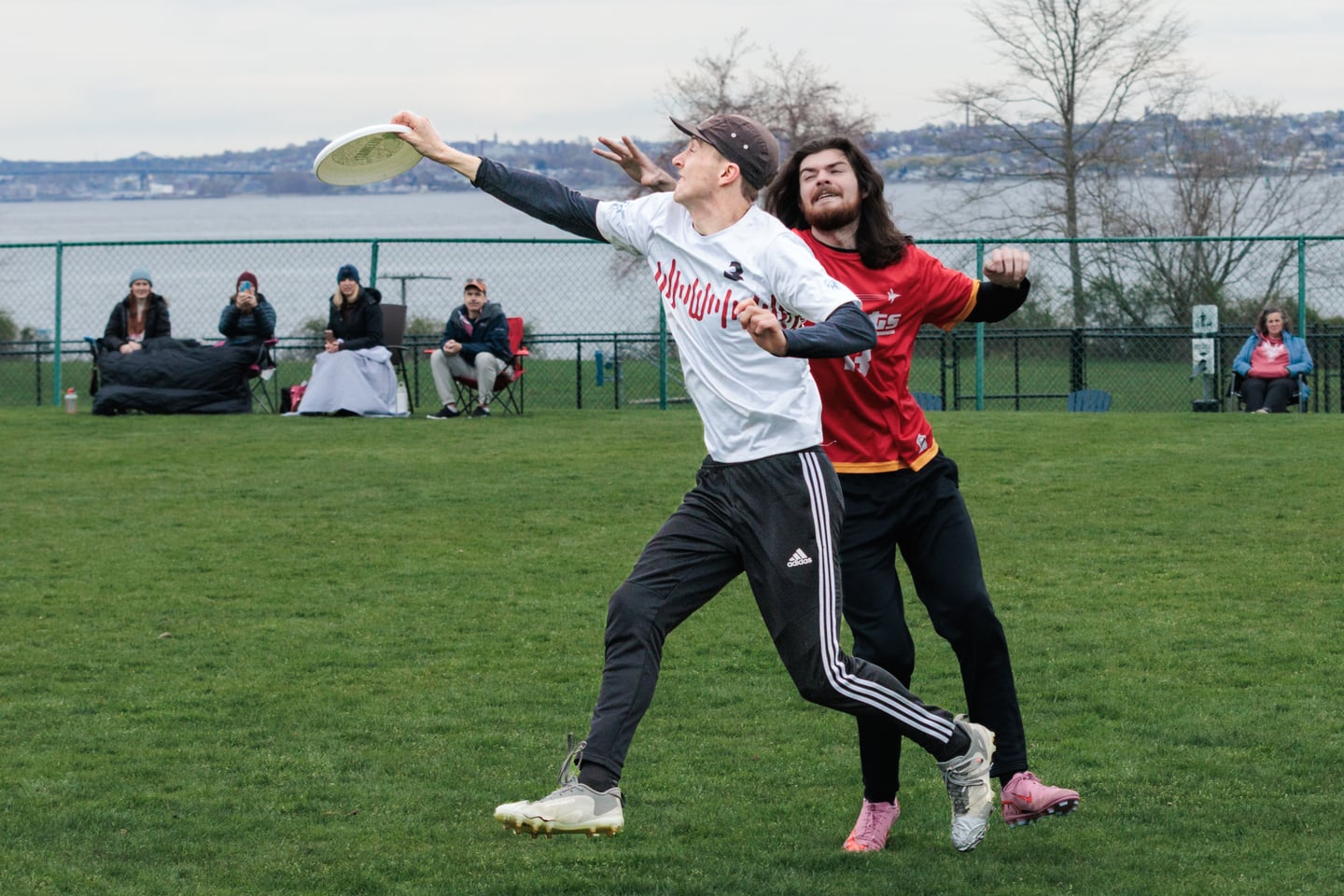 White-clad receiver extends both arms for the disc with a red-clad defender trailing.