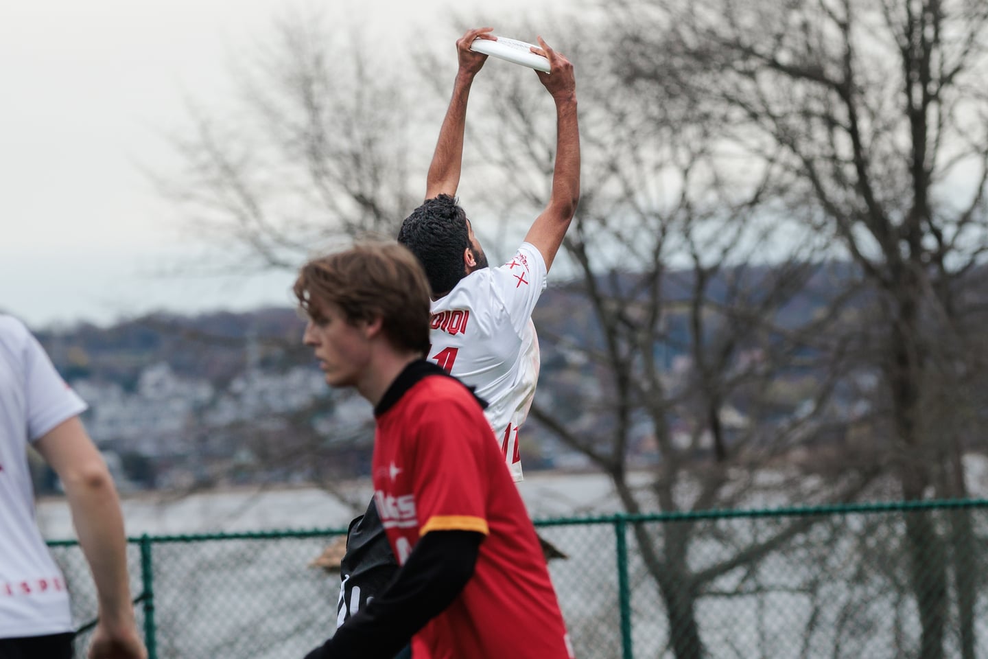 White-clad receiver secures the disc overhead beyond a red-clad opponent.