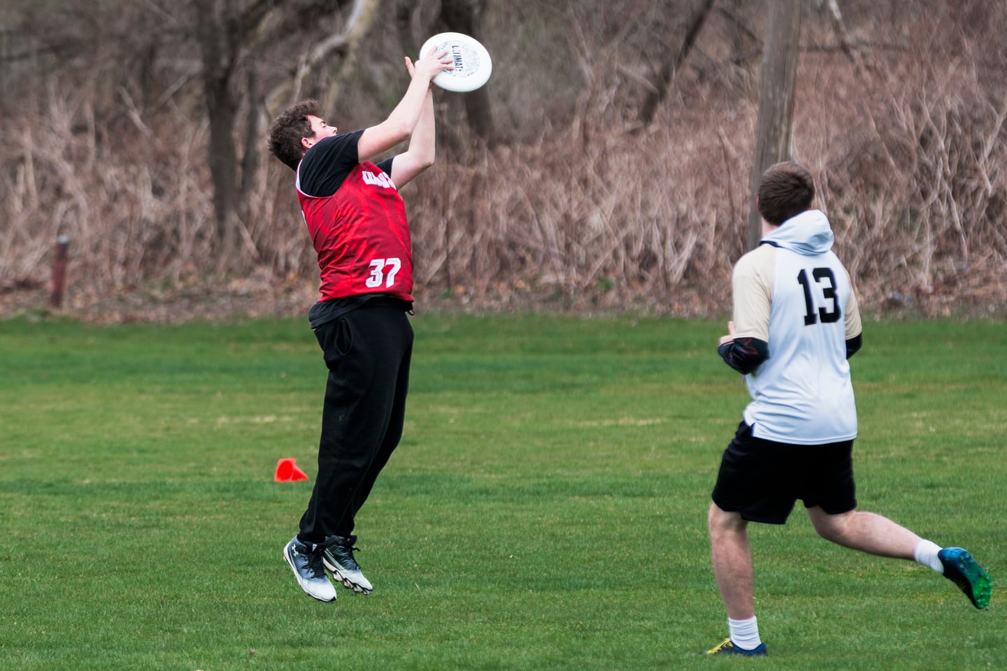 Red-clad player jumps overhead to catch a disc against a nearby defender.