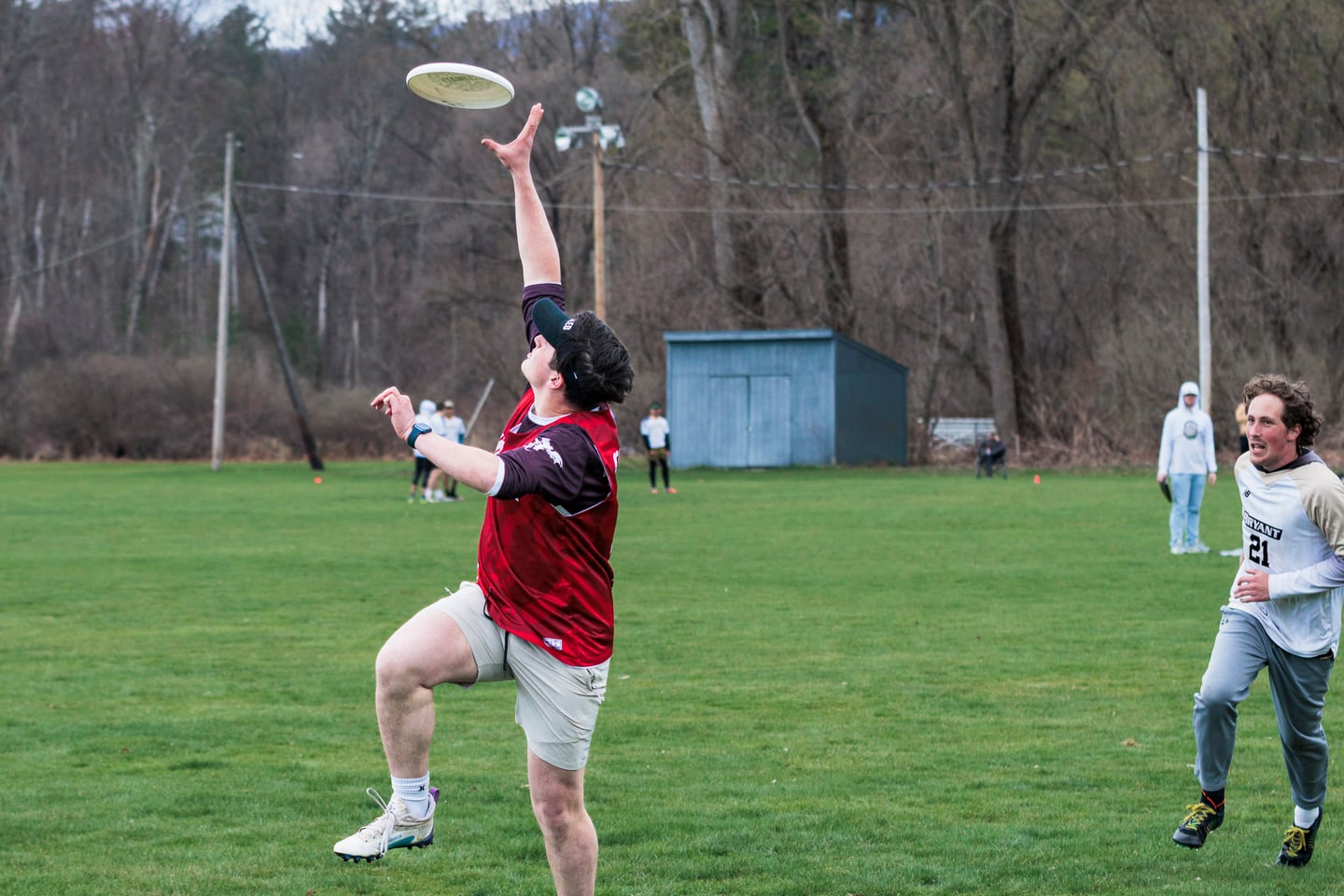 Red-clad player reaches overhead for a floating disc.