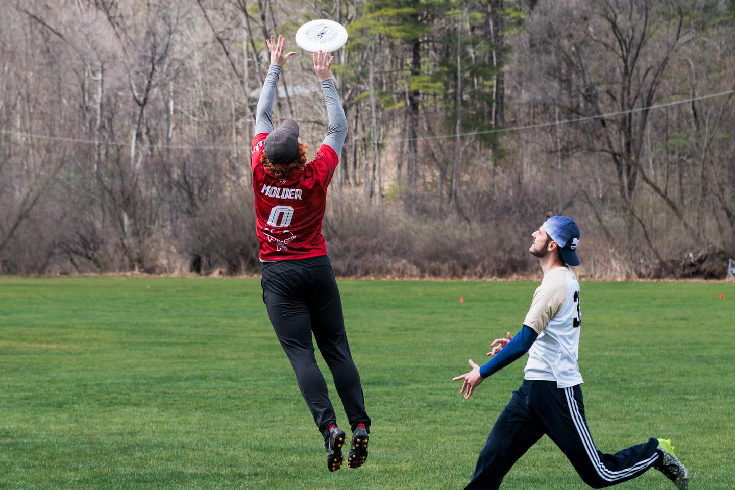 Red-clad player leaps vertically to catch a disc over a defender.