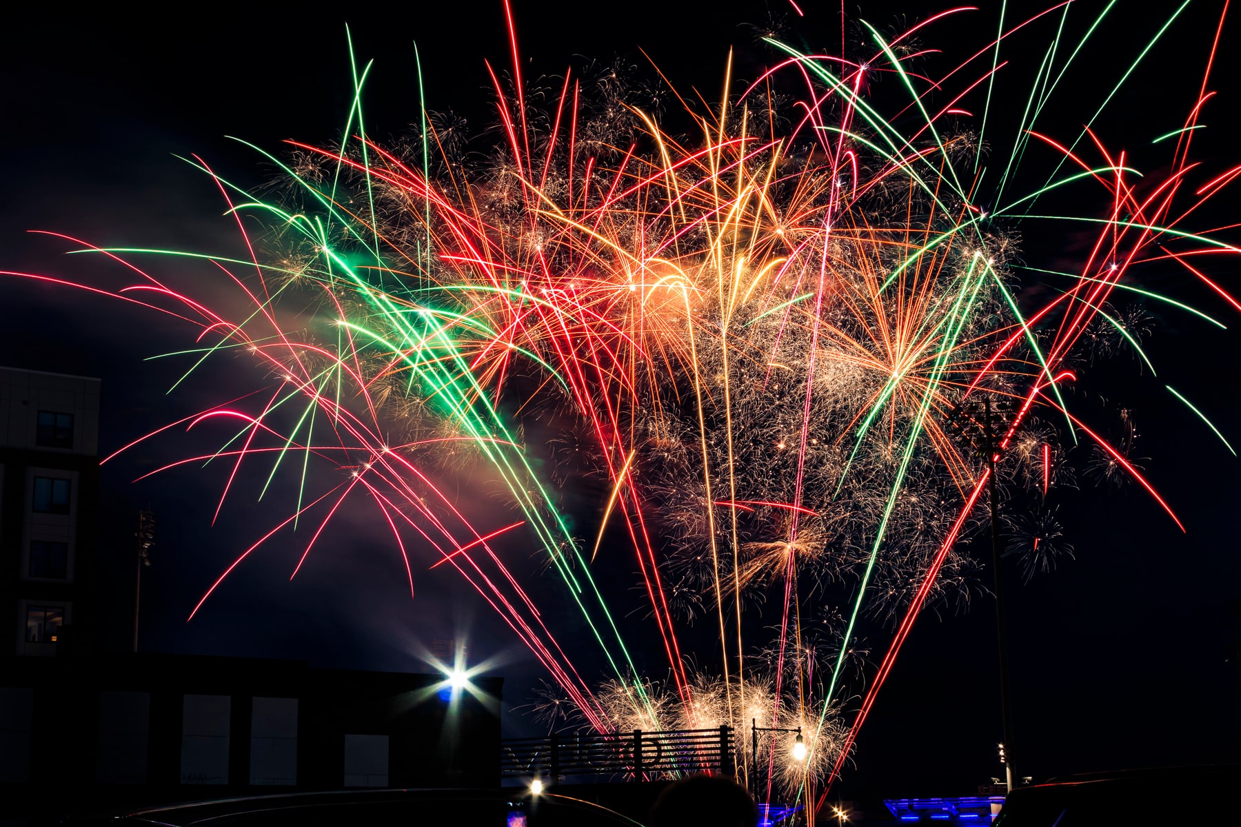 Red and green fireworks burst above a nighttime event as spectators watch from below.