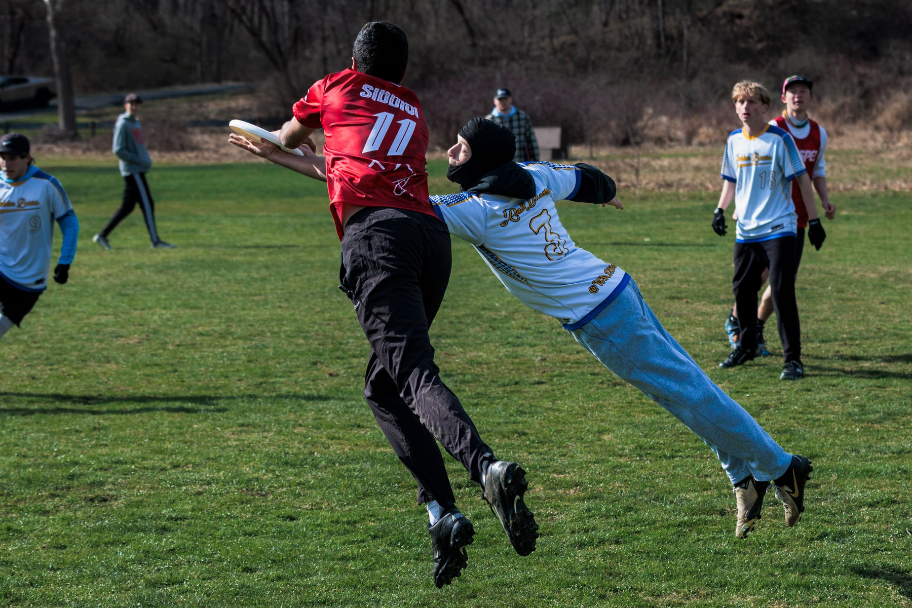 A defender lays out toward a red-shirted player holding the disc while other players watch the play develop.