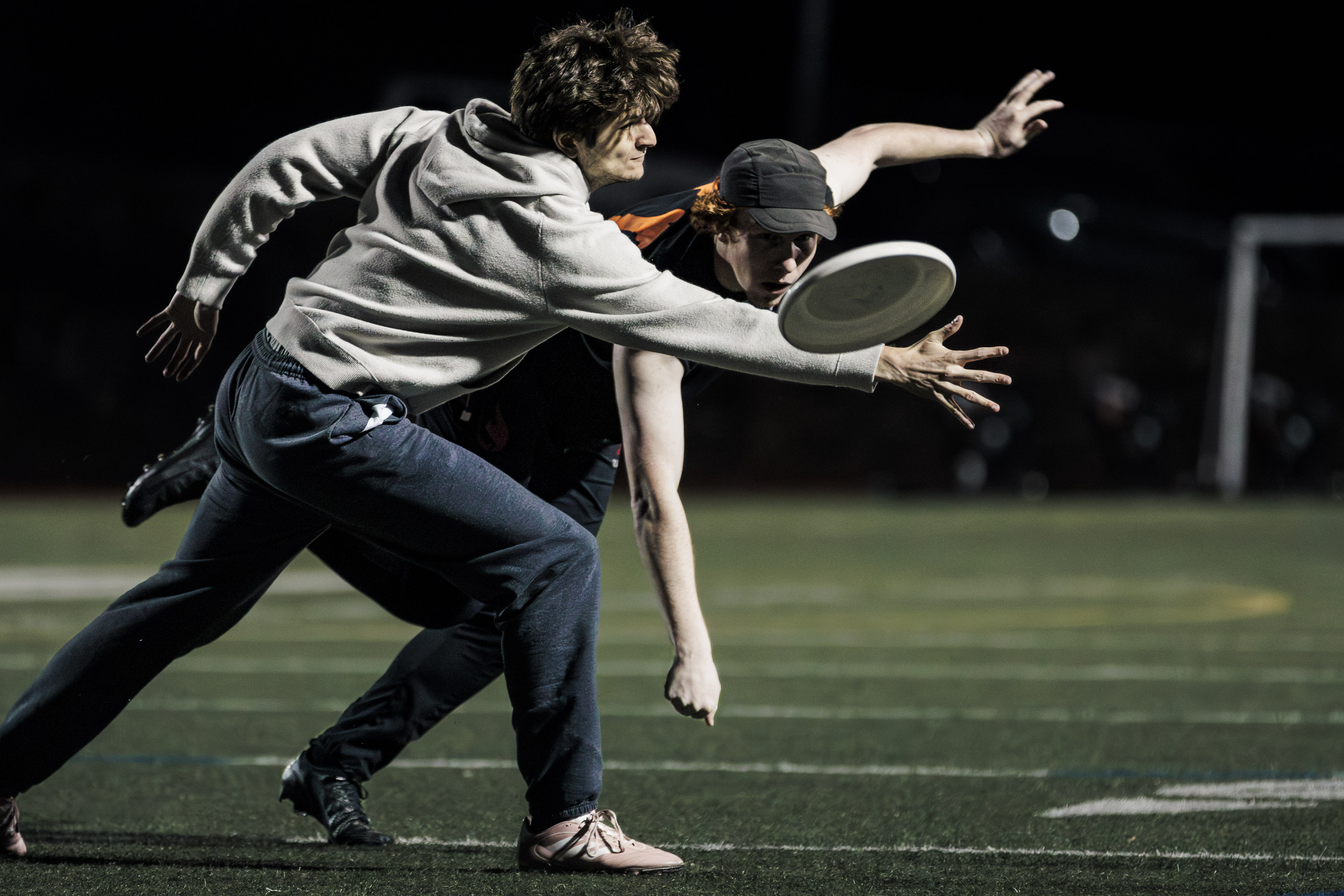 A player reaching for a flying disc under stadium lights.