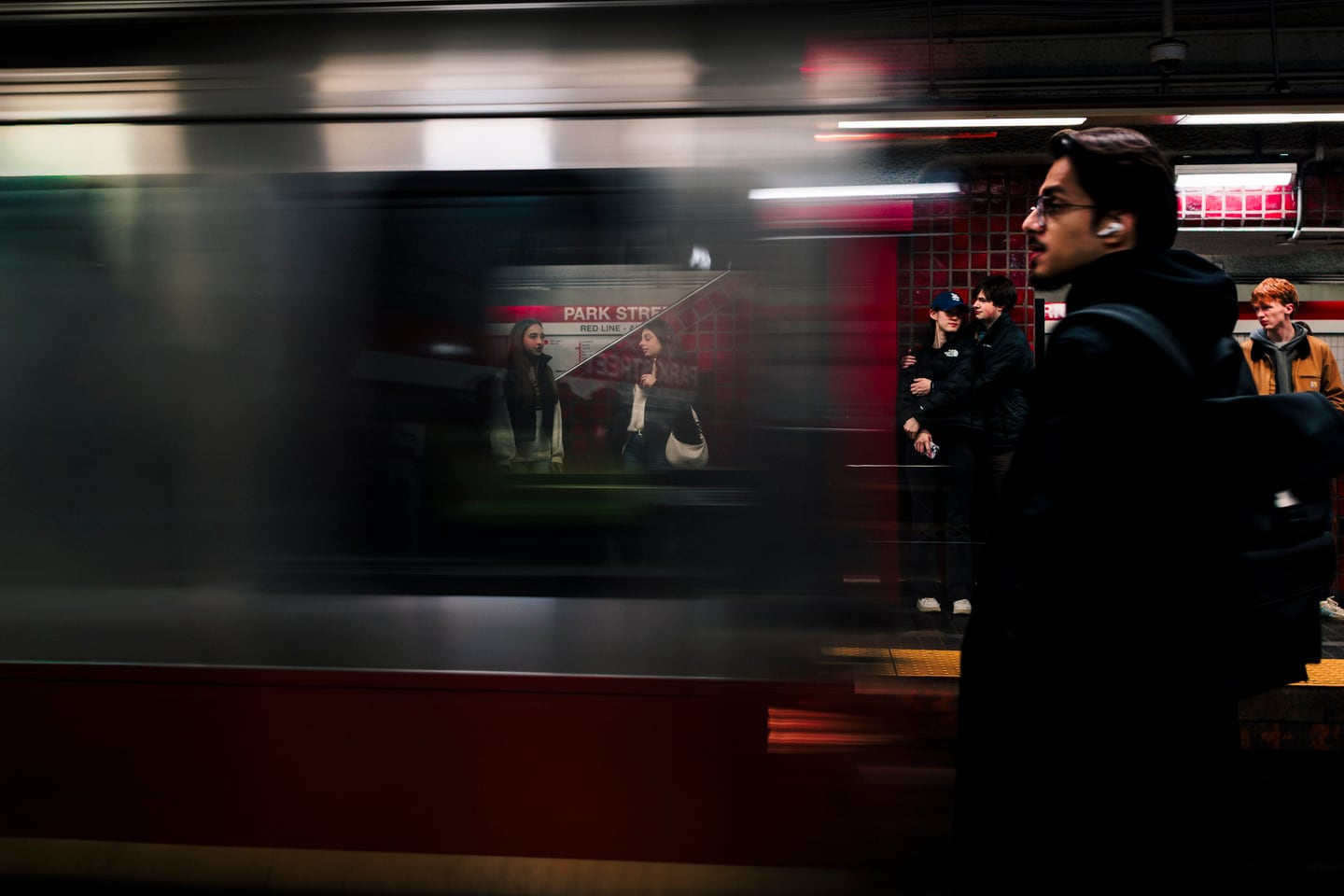 A red train passing through an urban street in motion.